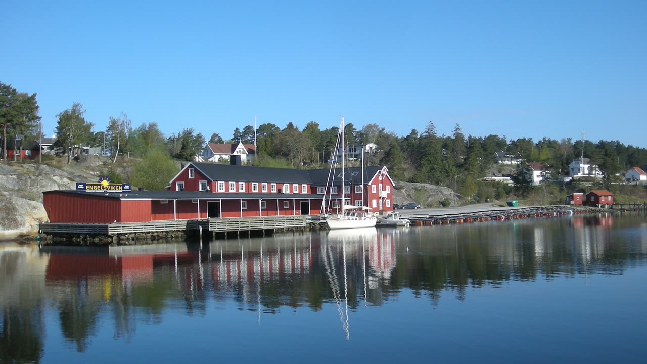 Engelsviken havn i Fredrikstad med røde sjøhus, seilbåt og brygge ved fjorden