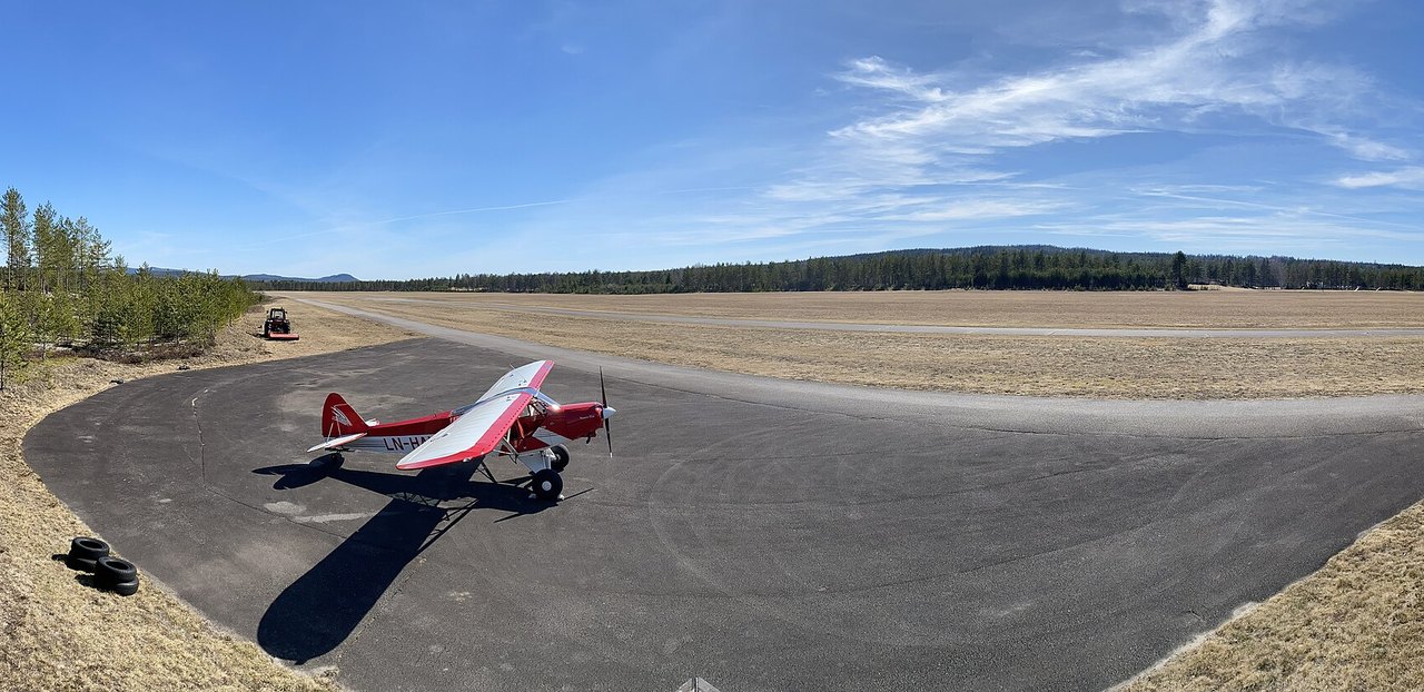 Rullebanen og oppstillingsplassen på Starmoen flyplass i Elverum, med et rødt småfly og skog i bakgrunnen