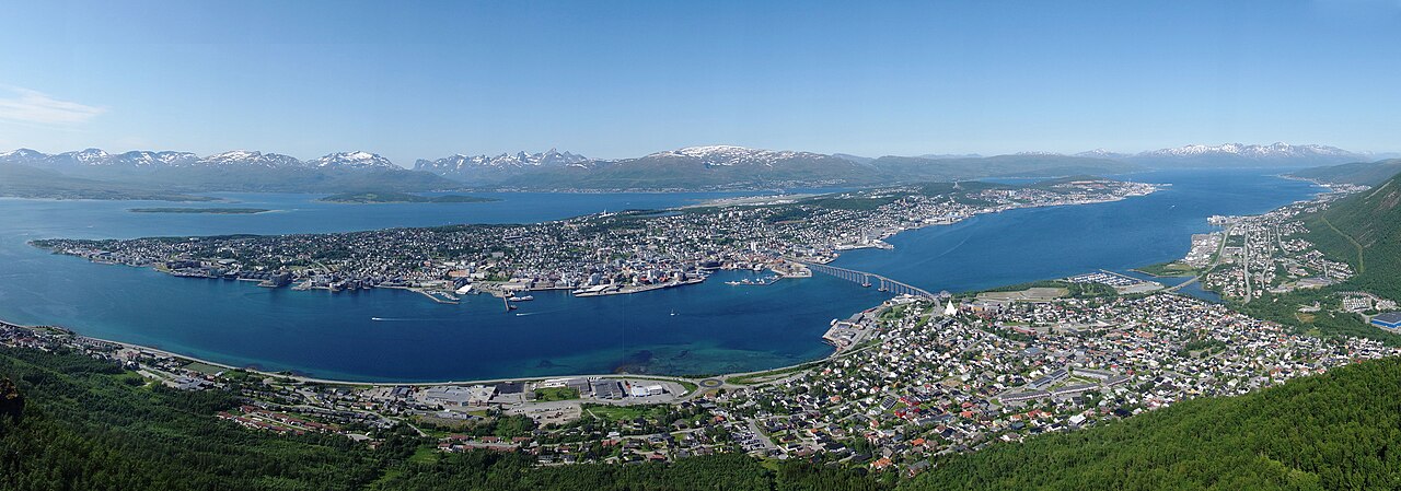 Panoramautsikt over Tromsø sett fra Fjellheisen med Ishavskathedralen og Tromsøbrua i forgrunnen, byøyas sentrum med havn i midten og fjellene på Kvaløya i bakgrunnen