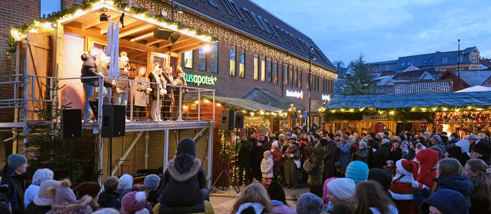 Julemarked i blåtimen med opplyst scene, lyslenker og publikum
