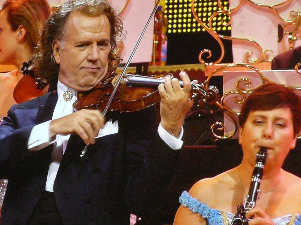 André Rieu spiller fiolin på scenen med orkesteret, en klarinettist i forgrunnen