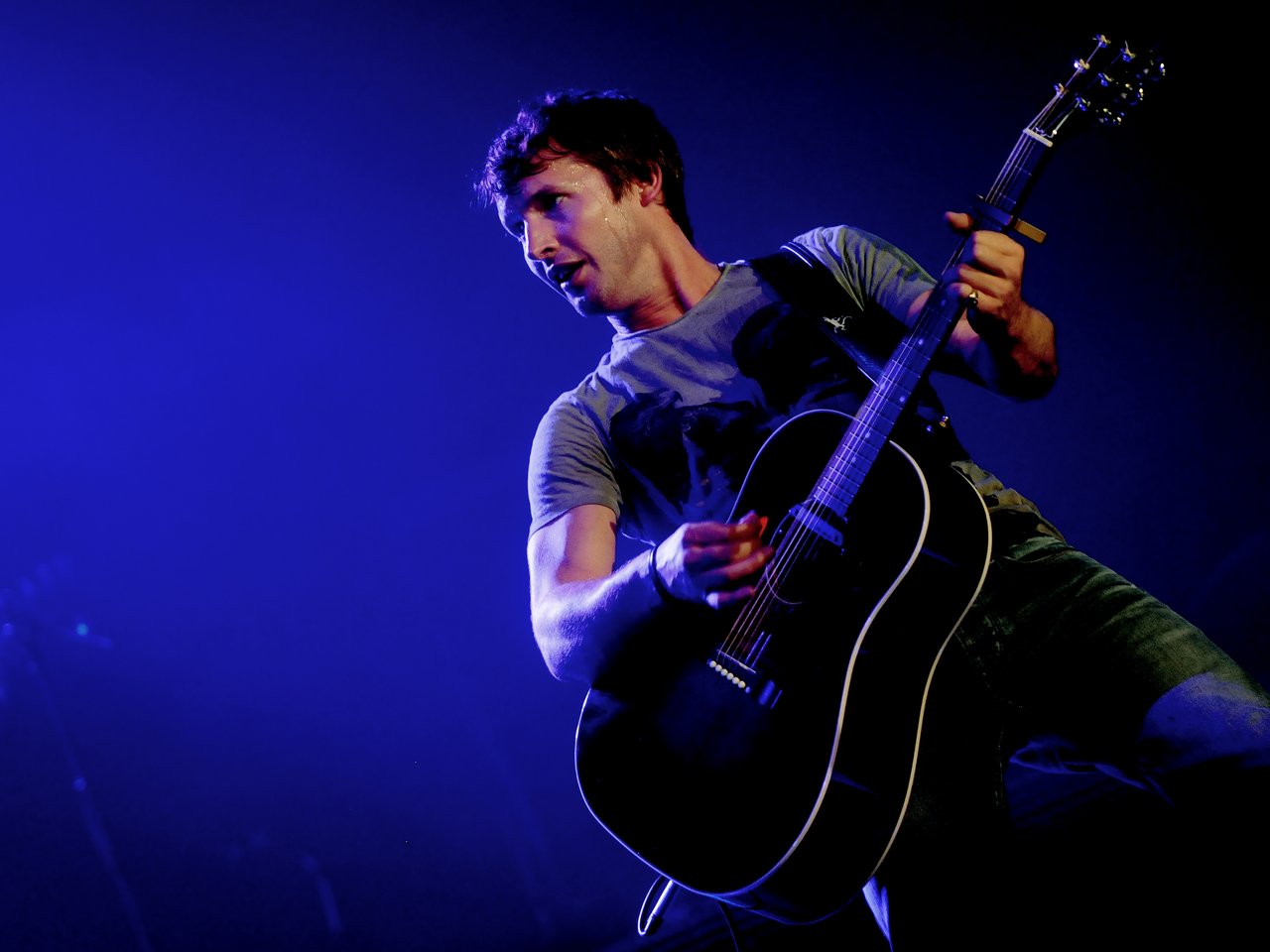 James Blunt med akustisk gitar på scenen i blått lys